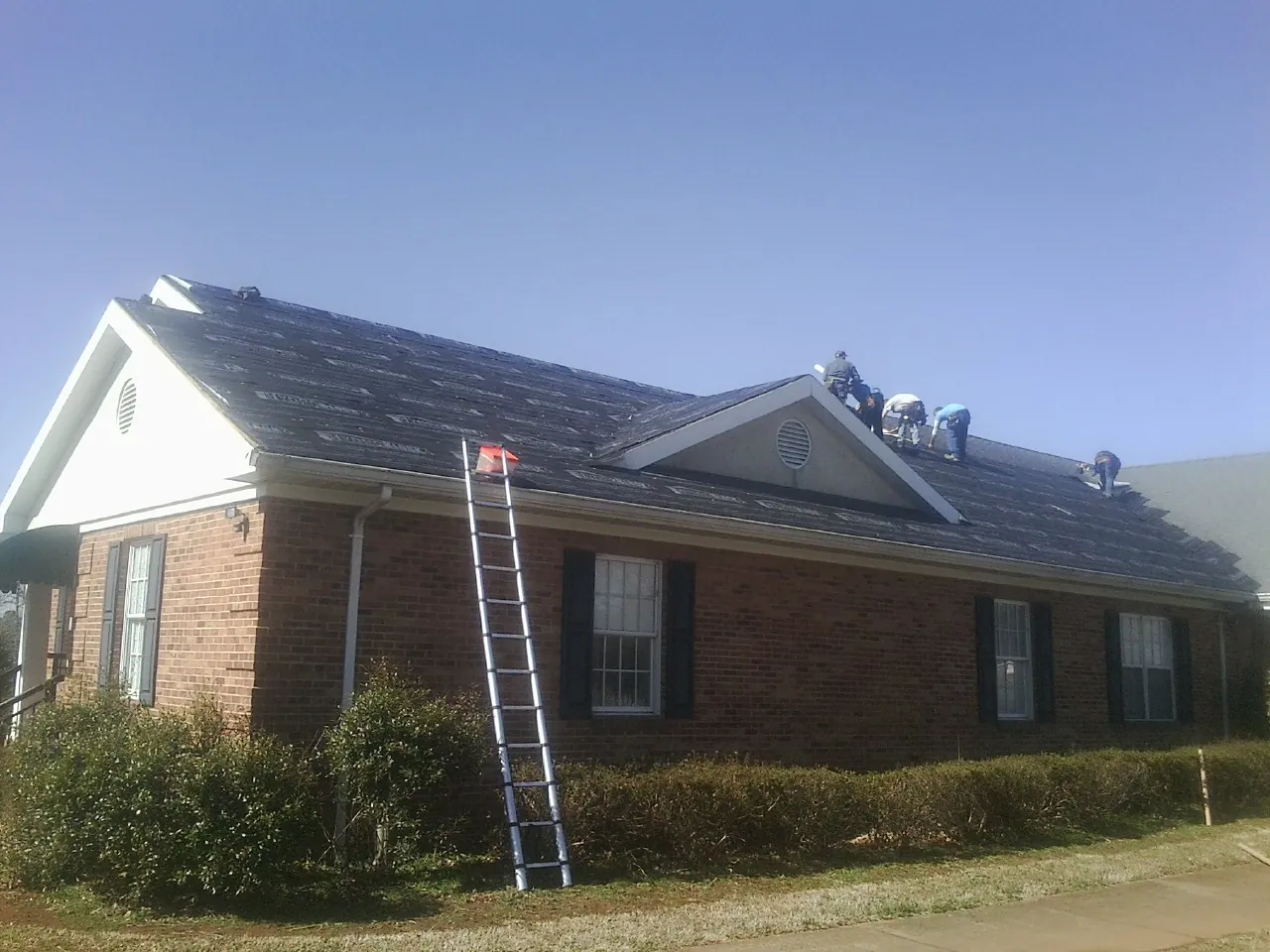 Crew tearing shingles off a brick ranch roof with a ladder set — Emergency Roof Repair work by our crew in Sierra Madre