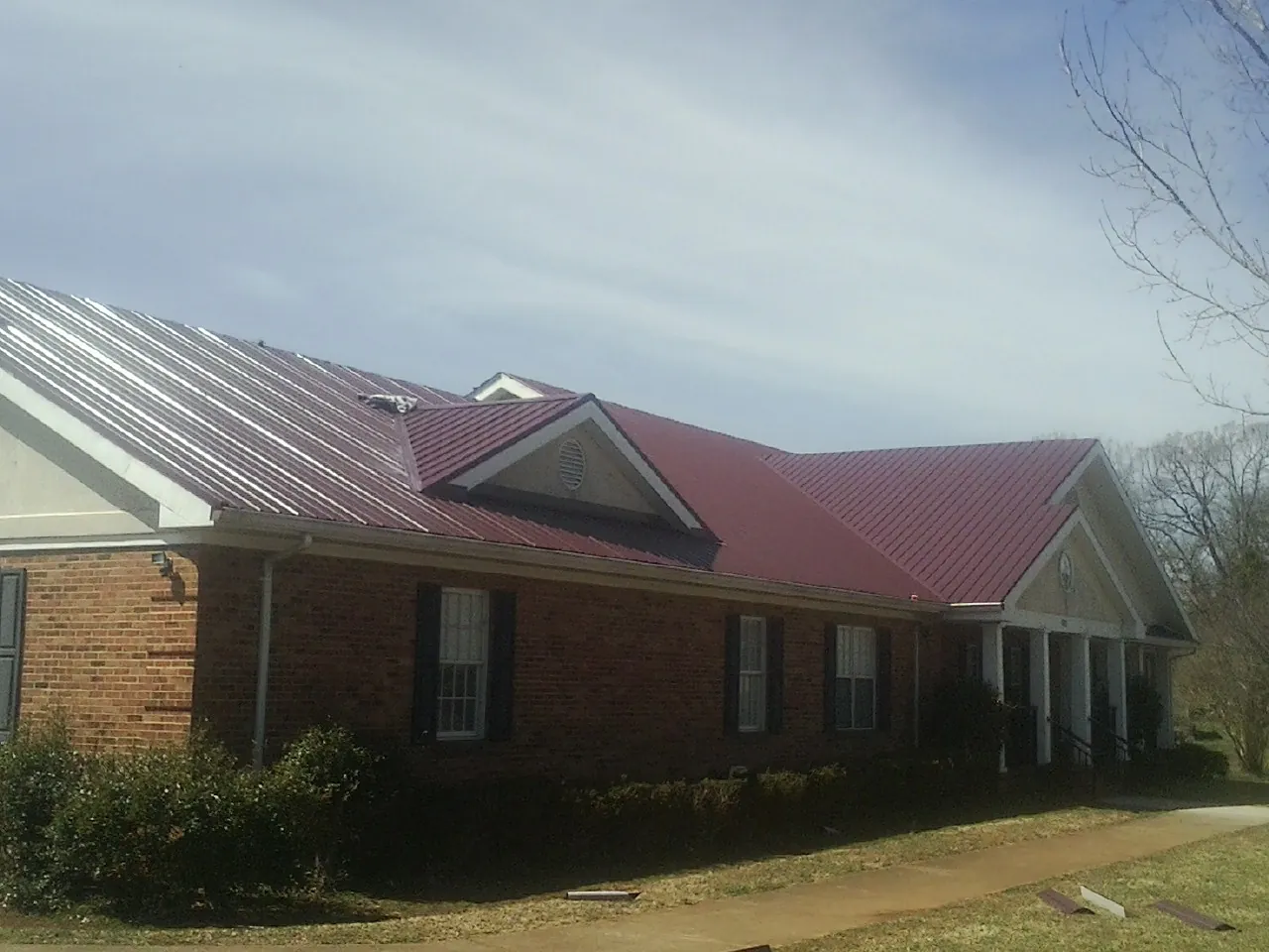 Red metal roof with gabled entries on a long brick building, from a Hail Damage Roof Repair job in Sierra Madre