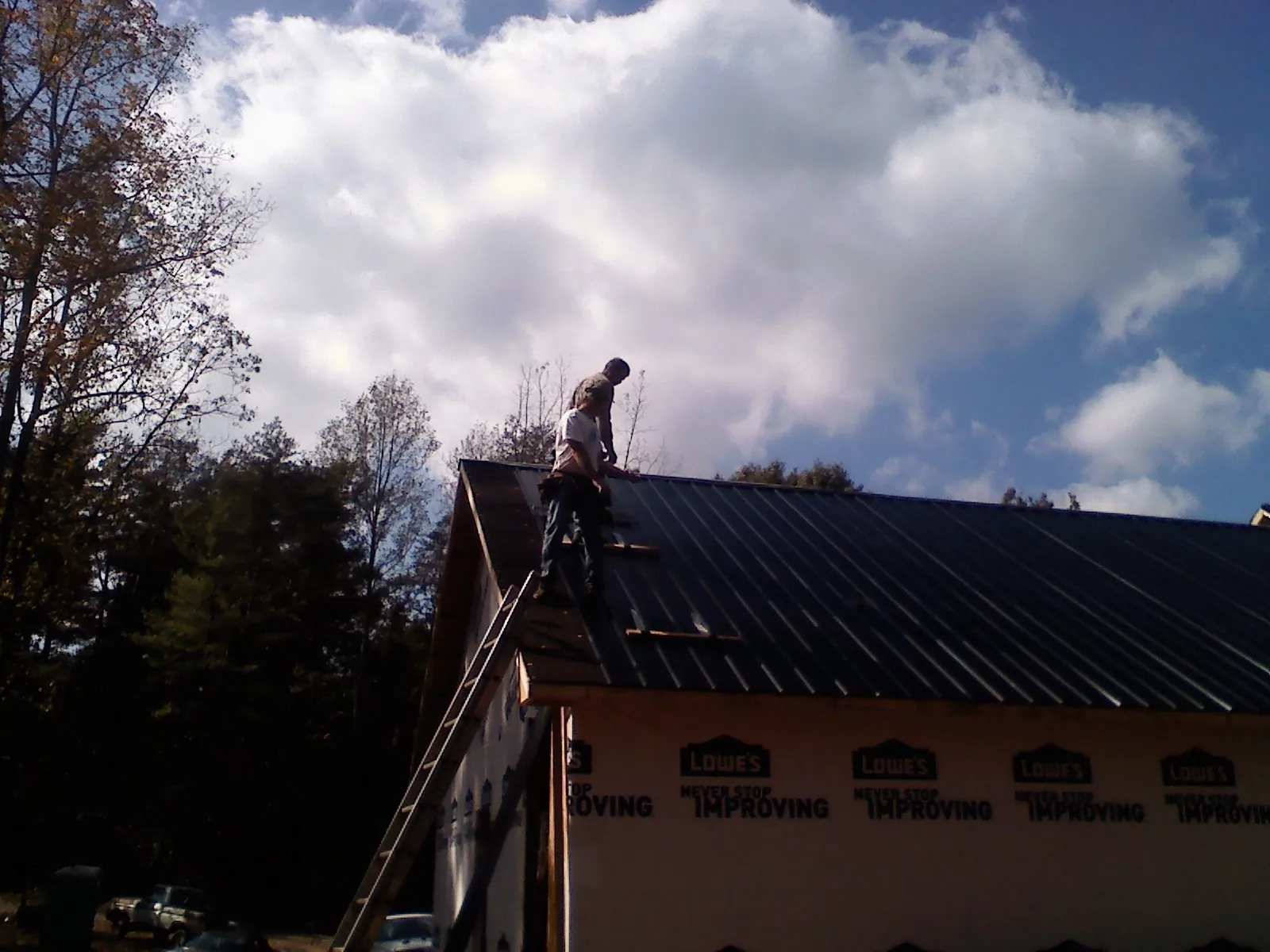 Roofer fastening dark metal panels high against a cloudy sky, from a Roof Inspection job in Sierra Madre
