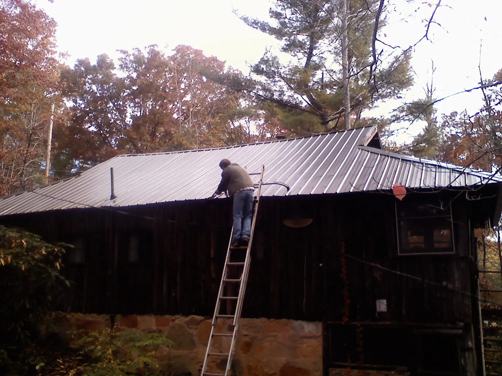 Roofer on a ladder working along the edge of a cabin metal roof in Sierra Madre