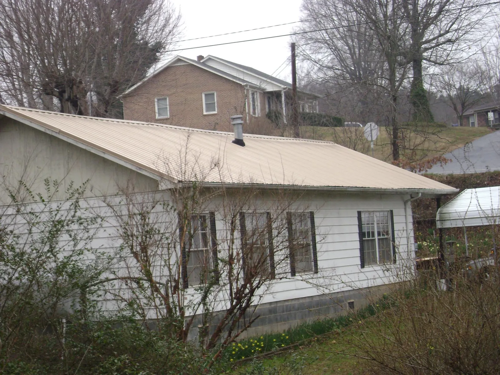 Tan metal roof on a white sided house set into a hillside — Commercial Roofing by Roofing Brothers in Sierra Madre